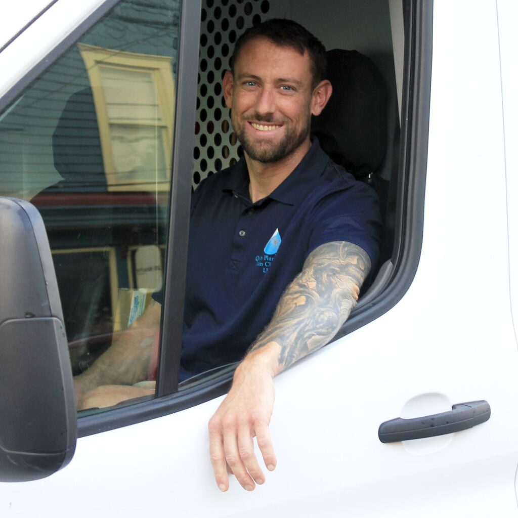 Master Plumber Kyle Leaper sits in the driver seat of his work truck, smiling at camera